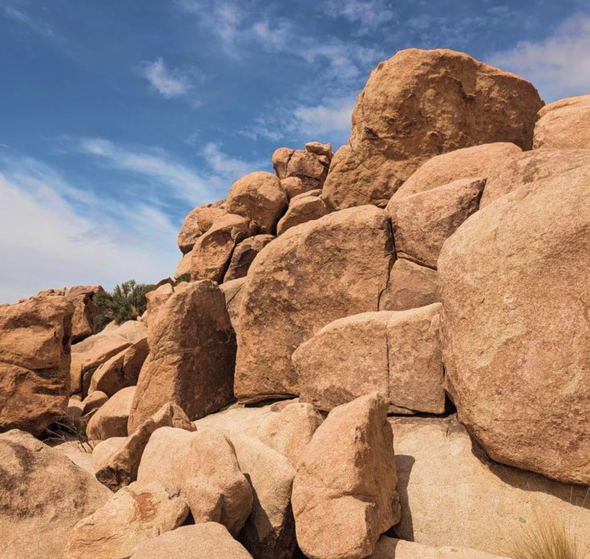A low-angle outdoor photograph of large tan rock boulders under a bright blue sky with light clouds.